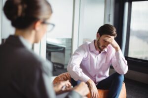 Man in therapy session with counselor, discussing mental health in a professional setting.